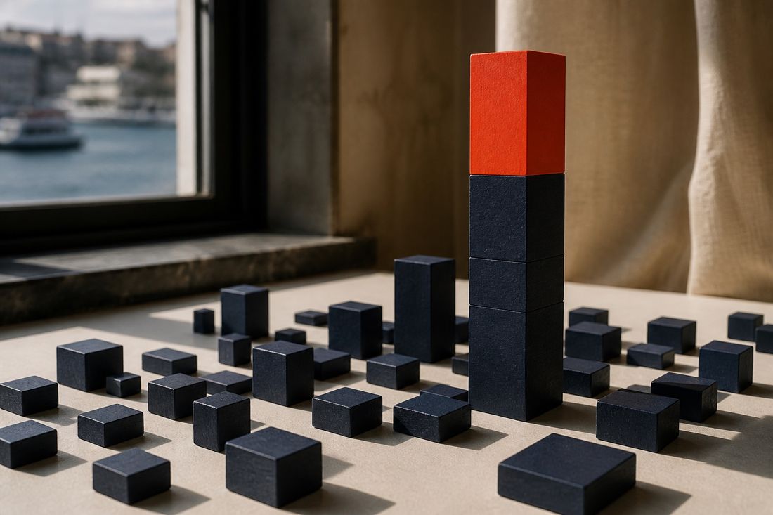 Many small navy blocks spread across a pale table with one tall stack rising among them, topped in red