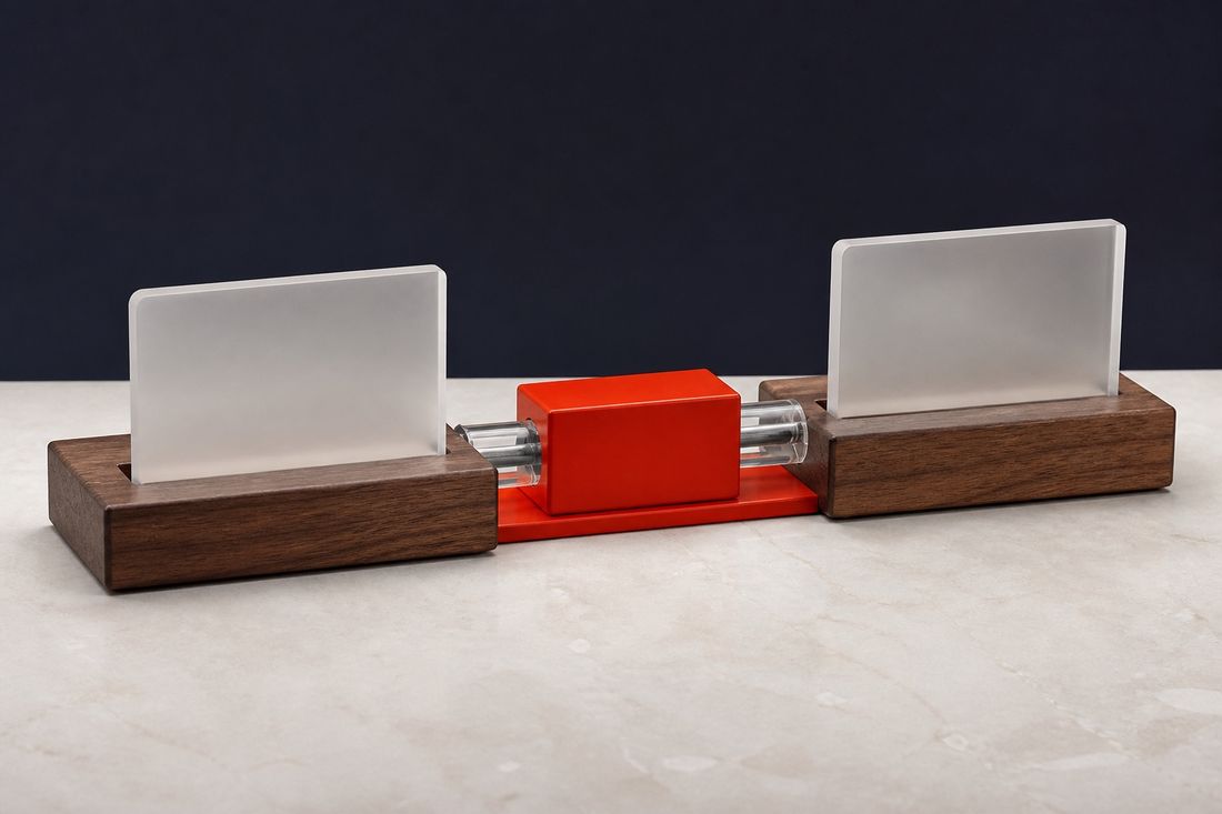 Two walnut stands holding frosted glass panels, joined by clear tubes that pass through a red block on pale marble
